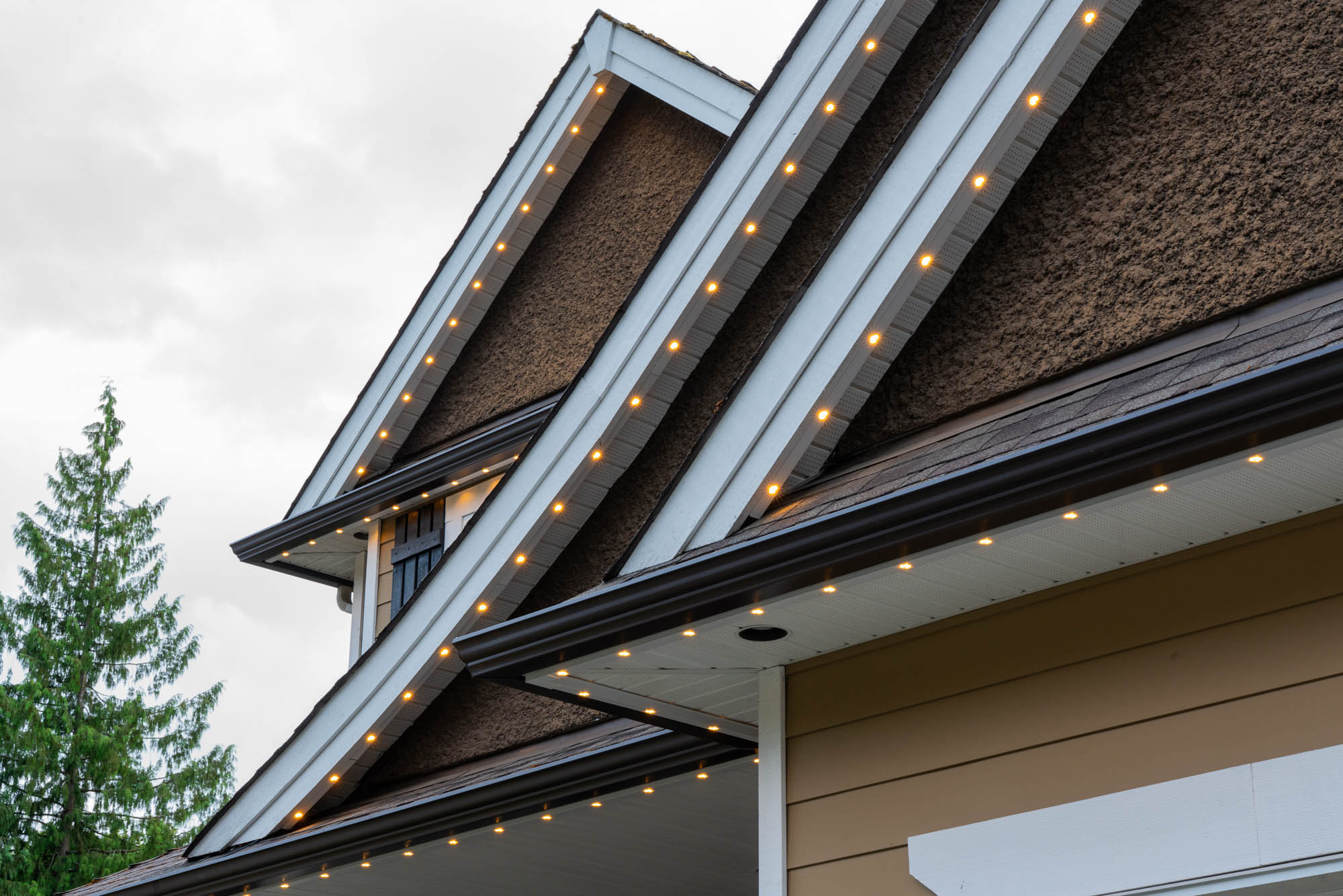 Permanent warm white roofline lighting on a multi-gable home at dusk in the West Kootenays
